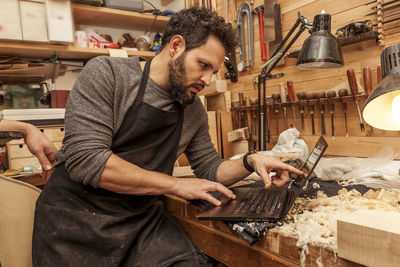 Two craftsmen violinmakers checking data and measures for a new violin with computer