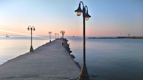 Street lights on pier by sea against sky during sunset