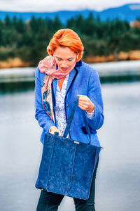 Woman looking at purse while standing by lake