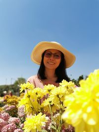 Portrait of smiling young woman with yellow flower against sky