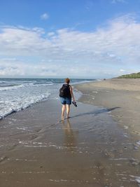 Rear view of woman walking on beach against sky