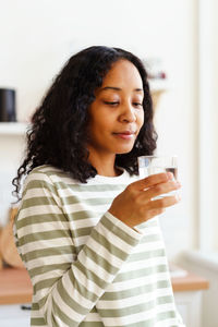 Smiling african-american female looking at glass of clear water on soft focused background