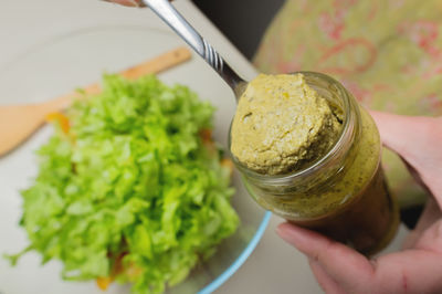 Woman's hand with a jar in the kitchen, from which salad sauce is taken out with a spoon