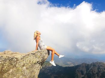 Side view of young woman on rock against sky