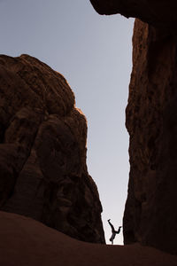 Silhouette person on rock formation against sky