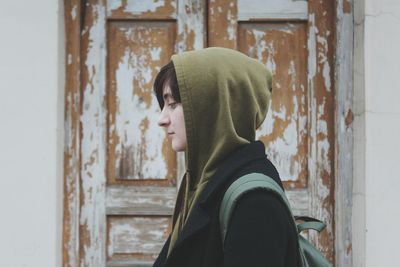 Side view of woman wearing hooded shirt against house