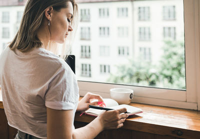 Young business woman is working near the window and uses your laptop and notepad. 