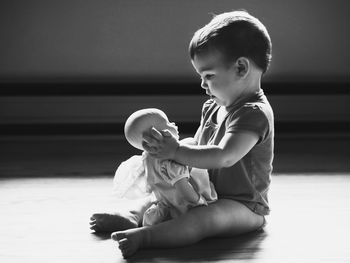 Side view full length of baby girl playing with doll on floor