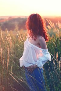 Rear view of woman standing on field during sunset