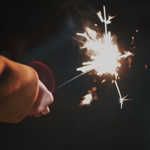 Cropped hand holding sparkler at night