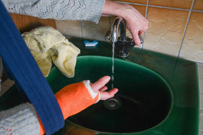 Woman with broken arm in cast checks the temperature of the tap water for washing her hands, the