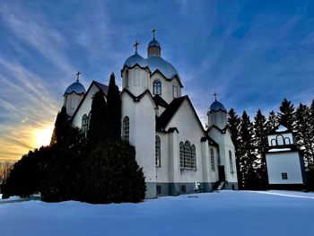 Church by building against sky during winter