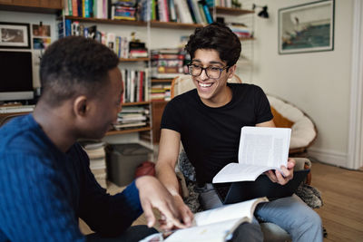 Cheerful friends studying while sitting in living room at home