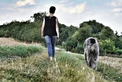 Rear view of man with dog walking on field