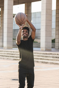 Smiling young man playing basketball in park during sunset