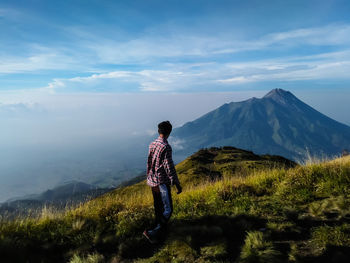 Hiker walking on mountain against cloudy sky