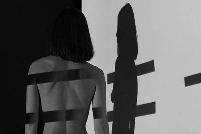 Rear view of shirtless woman standing by wall