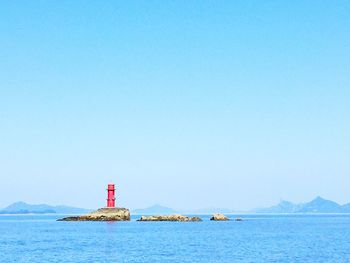 Lighthouse by sea against clear blue sky