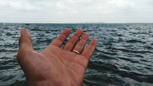 Close-up of hand over sea against sky