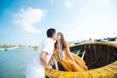 Couple kissing in boat at beach against sky