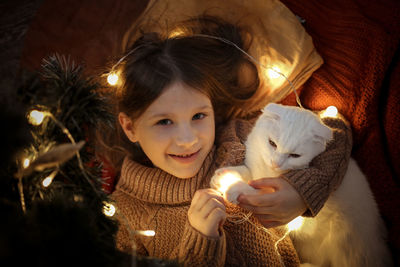 Cozy girl and domestic cat are under the christmas tree, dark golden style. 