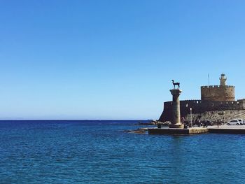 Statue by sea against clear blue sky