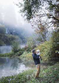 A man is holding a baby near a river