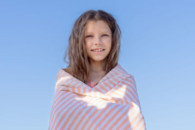 Portrait of a young girl wrapped in a towel against the blue sky.
