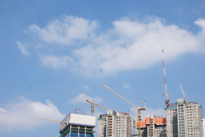 Low angle view of crane and buildings against sky