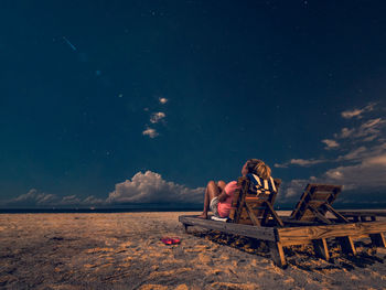 People sitting on beach against sky at night