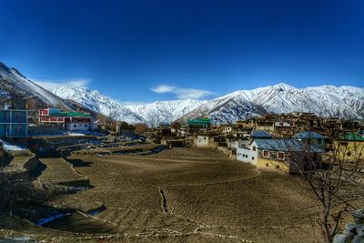 Snow covered houses by buildings against blue sky