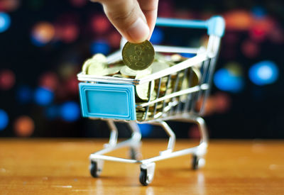 Close-up of person holding coin over shopping cart on table
