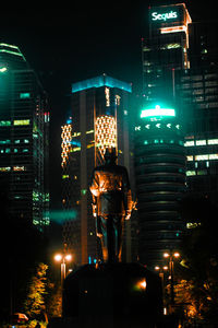 Rear view of man standing by illuminated buildings at night