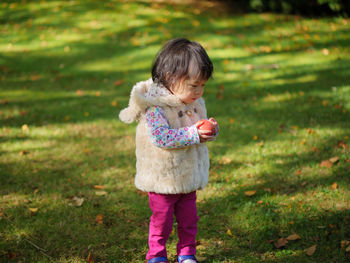 Baby girl holding apple while standing on grassy field