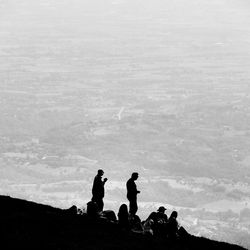 Silhouette people on rocks against sky