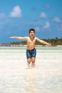 Funny kid running throw the water of a beach with open arms