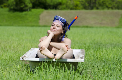 Portrait of woman sitting in old bathtub on grassy field