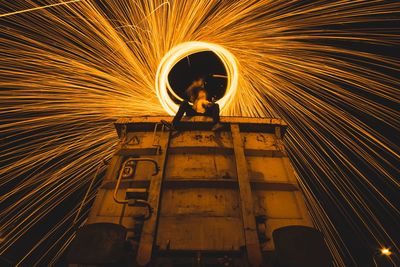 Low angle view of person sitting on train while spinning fire steel wool at night