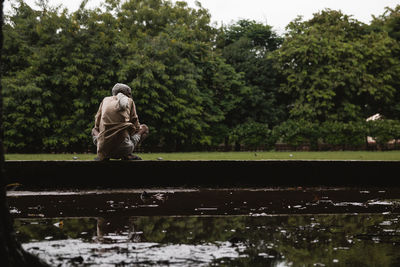 Rear view of man crouching by pond in park