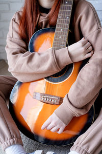 Young caucasian red-haired woman sitting on rug and playing acoustic guitar at home