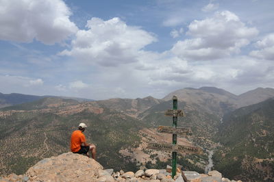 Rear view of man sitting on rock against sky