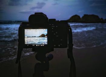 Reflection of camera on mobile phone at beach against sky