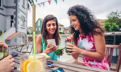 Friends using mobile phone while having smoothie at restaurant