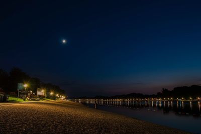 View of illuminated beach against sky at night