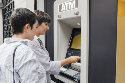 Young woman with girlfriend using atm machine