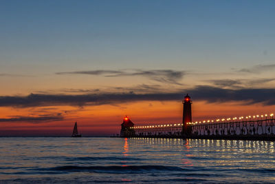 A sailboat approaches the lighthouse in grand haven, michigan, at sunset on lake michigan