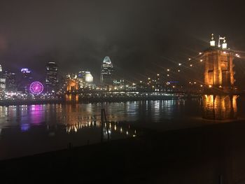 Illuminated buildings by river against sky at night