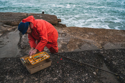 Man searching for fishing bait in container while standing by sea