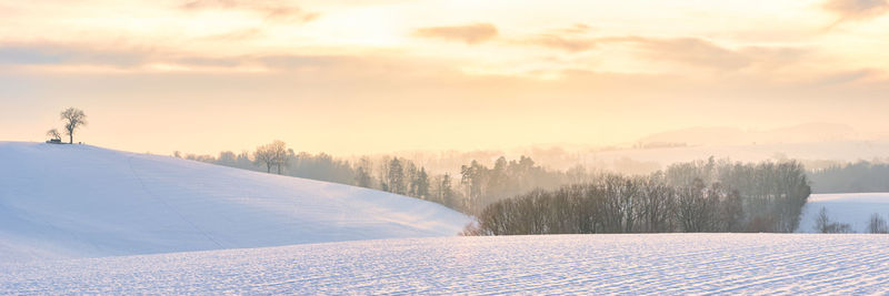 Snow covered field against sky during sunset