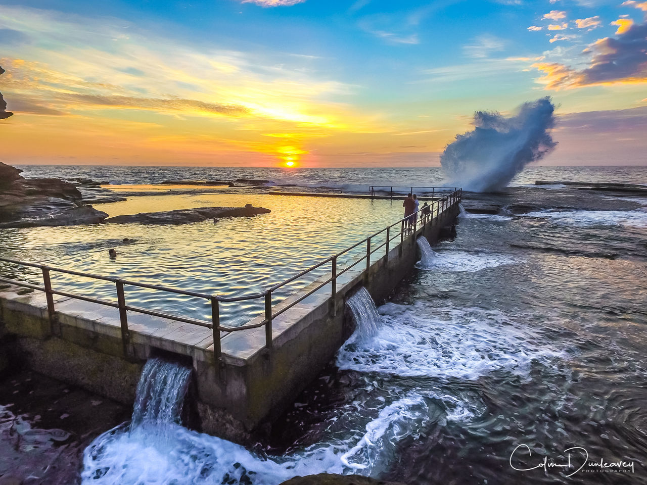 water, motion, sunset, scenics, environment, orange color, surf, sea, power in nature, flowing, beauty in nature, flowing water, long exposure, wave, splashing, tranquil scene, nature, sky, idyllic, cloud - sky, railing, travel destinations, sun, tranquility, dramatic sky, wake - water, non-urban scene